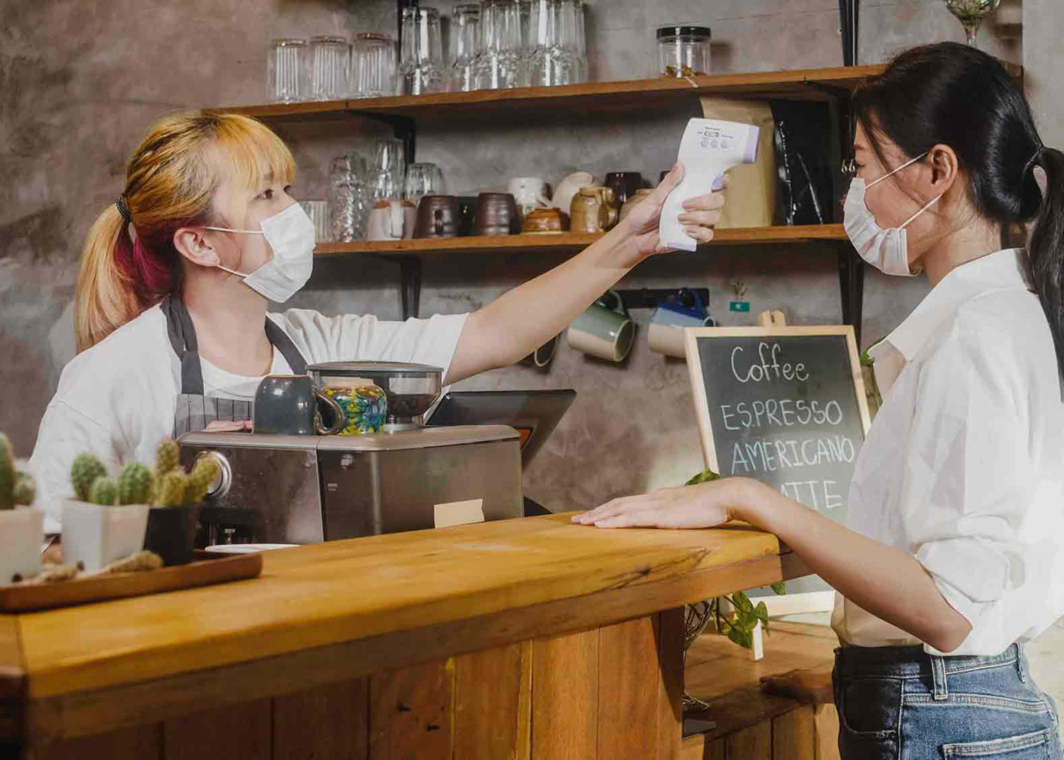 Restaurant staff using infrared thermometer checker with customer